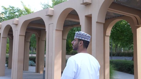 الخروج إلى أحد الاماكن العامة للترفيه عن النفس، الاستجمام بالطبيعة واستنشاق الهواء الطلق، الاستمتاع بالأجواء في إحدى المنتزهات، رجل عربي خليجي عماني يرتدي الزي العماني يسير فى احدي حدائق سلطنة عمان