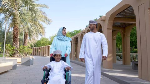 نزهة وجولة فى الهواء الطلق، زوجان عربيان خليجيان عمانيان مستمتعان برفقه ابنهم، قضاء اوقات ممتعه مع العائله ، تصوير لعائلة عربية خليجية عمانيه تجلس فى الحديقة ، ولد يجلس على كرسي متحرك
