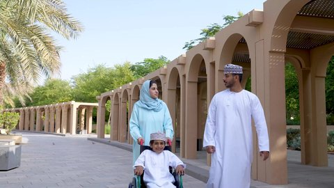 زوجان عربيان خليجيان عمانيان مستمتعان برفقه ابنهم، قضاء اوقات ممتعه مع العائله ،نزهة وجولة فى الهواء الطلق، تصوير لعائلة عربية خليجية عمانيه تجلس فى الحديقة ، ولد يجلس على كرسي متحرك