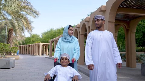 قضاء اوقات ممتعه مع العائله ،نزهة وجولة فى الهواء الطلق، تصوير لعائلة عربية خليجية عمانيه تجلس فى الحديقة ، ولد يجلس على كرسي متحرك ، زوجان عربيان خليجيان عمانيان مستمتعان برفقه ابنهم