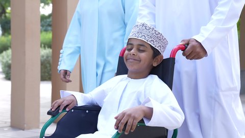 تصوير لعائلة عربية خليجية عمانيه تجلس فى الحديقة ، ولد يجلس على كرسي متحرك ، زوجان عربيان خليجيان عمانيان مستمتعان برفقه ابنهم، قضاء اوقات ممتعه مع العائله ،نزهة وجولة فى الهواء الطلق