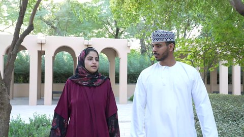 Smiling Omani Gulf Arab couple walking together on a pleasant outing to one of the entertainment places, outing during vacation time, participating in fun activities, spending enjoyable family time
