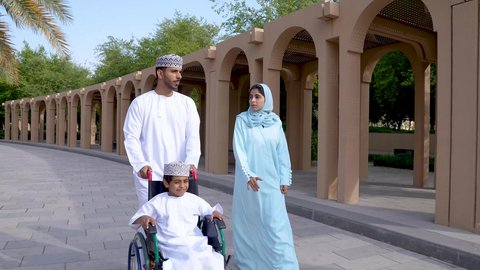 قضاء اوقات ممتعه مع العائله ، تصوير لعائلة عربية خليجية عمانيه تجلس فى الحديقة ، نزهة وجولة فى الهواء الطلق، ولد يجلس على كرسي متحرك  ، زوجان عربيان خليجيان عمانيان مستمتعان برفقه ابنهم