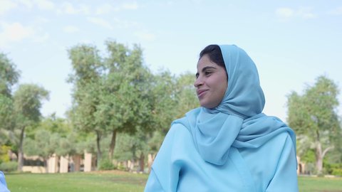 إيماءات الفرح والسرور،اجواء الطبيعة الخلابة، قضاء أوقات ممتعة ,سيدة عربية خليجية عمانية ترتدي العباءه والحجاب تجلس في الحديقة  , ممارسة الأنشطة الترفيهية , خلفية الطبيعة