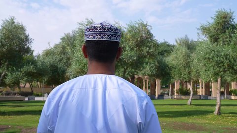 الاستمتاع بالأجواء في إحدى المنتزهات، الاستجمام بالطبيعة واستنشاق الهواء الطلق، تصوير من الخلف لطفل عربي خليجي عماني يرتدي الزي العماني يسير فى احدي حدائق سلطنة عمان ،الخروج إلى أحد الاماكن العامة للترفيه عن النفس