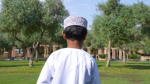الاستجمام بالطبيعة واستنشاق الهواء الطلق، الاستمتاع بالأجواء في إحدى المنتزهات، تصوير من الخلف لطفل عربي خليجي عماني يرتدي الزي العماني يسير فى احدي حدائق سلطنة عمان ،الخروج إلى أحد الاماكن العامة للترفيه عن النفس