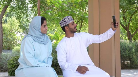 الجلوس في الهواء الطلق و الطبيعة الخضراء, زوجان عربيان خليجيان عمانيان يقومان بإلتقاط صور سيلفي تذكارية بإستخدام الهاتف المحمول, التنزه في حدائق سلطنه عمان, أنشطة عائلية ترفيهية