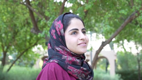 امرأه سعوديه ترتدي عباءه وحجاب في وضح النهار وسط جو هادئ ومنعش، سيده عمانيه تقف في مكان طبيعي تحيط به الأشجار الخضراء، التنزهه في الهواء الطلق، ايماءه التمعن والتركيز