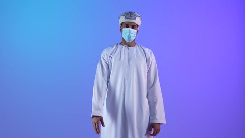 إلقاء التحيه والسلام, مفهوم الاستقبال والترحيب, التعارف و الصداقه وتكوين علاقات، بورتريه لرجل عربي خليجي عماني يرتدي الدشداشة والكمه يقوم بالمصافحة، ارتداء الكمامة لإجراءات الوقاية من فايروس كورونا خلفية زرقاء