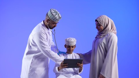 مراجعة وتشخيص حالة المريض ، مهن ووظائف طبية ، تصوير لأم خليجية عمانيه مع طفلها الصغير في زيارة الى دكتور الأطفال ، موعد مع الطبيب لتلقي العلاج ، إستخدام جهاز التابلت ، مفهوم الطب والرعاية الصحية ، الفحص الطبي للأطفال ، تقديم الرعاية والخدمات الصحية