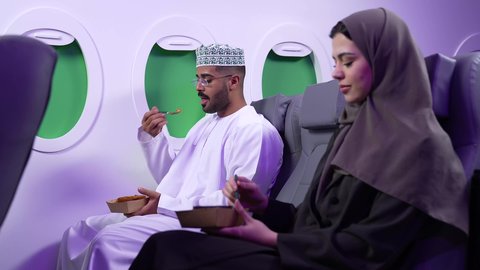 أجواء عائليه سعيده، الاستعداد لتناول الطعام مع الاهل، تصوير مقرب من الجانب لرجل وامراه عربييان خليجييان عمانييان يرتديان الزى العماني يجلسان على كرسيان داخل الطائره يتشاركان الطعام ، مأكولات ومشروبات سريعه وجاهزه، طيران عمان