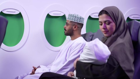 مفهوم الأمومة والطفولة ، إيماءات وجه مختلفة تدل على الحب والأمان، تصوير مقرب من الجانب لرجل وامراه عربييان خليجييان عمانييان يرتديان الزى العماني يجلسان على كرسيان داخل الطائره ، اجواء عائليه دافئه ،  الأسرة وتحمل المسؤولية