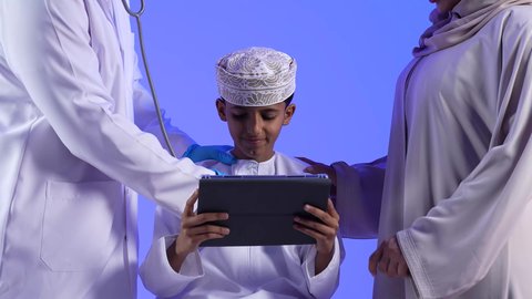 مهن ووظائف طبية ، مراجعة وتشخيص حالة المريض ، تصوير لأم خليجية عمانيه مع طفلها الصغير في زيارة الى دكتور الأطفال ، موعد مع الطبيب لتلقي العلاج ، إستخدام جهاز التابلت ، مفهوم الطب والرعاية الصحية ، الفحص الطبي للأطفال ، تقديم الرعاية والخدمات الصحية