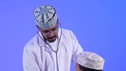 تقديم الرعاية والخدمات الصحية ، تصوير لطبيب خليجي عماني مع طفل صغير ، مفهوم الطب والرعاية الصحية ، الفحص الطبي للأطفال ، مهن ووظائف طبية ، يفحص الطبيب قلب الطفل عبر سماعة الأذن ، موعد مع الطبيب لتلقي العلاج