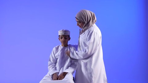 تقديم الرعاية والخدمات الصحية ، الفحص الطبي للأطفال ،تصوير لطبيبة خليجية عمانيه مع طفل ، مفهوم الطب والرعاية الصحية ، مهن ووظائف طبية ، تفحص الطبيبة حالة المريض عبر سماعة الأذن ، موعد مع الطبيب لتلقي العلاج ، تشخيص حالة المريض