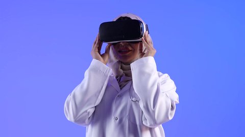 مفهوم الطب والرعاية الصحية ، إستخدام التقنيات الإلكترونية الحديثة ، تصوير لطبيبة عربية خليجية سعودية ترتدي نظارات الواقع الإفتراضي (في آر) ثلاثية الأبعاد ، مهن ووظائف طبية ، النظر من خلال نظارات الواقع الإفتراضي بإيماءات وجه ويدين مختلفة
