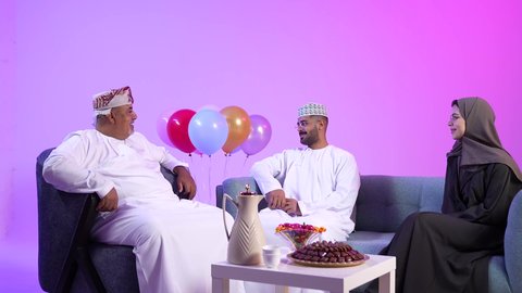 إظهار مشاعر الفرح والسعادة بقدوم العيد، تقديم التمر السعودي ، تجمع العائلة العمانية لاستقبال العيد المبارك, تقديم الضيافة العربية والحلويات الشعبية، تبادل المعايدات, مفهوم الحنان والمحبة والمودة، تصوير لعائلة عربية خليجية عمانية تجلس في غرفة المعيشة بايماءات السعادة