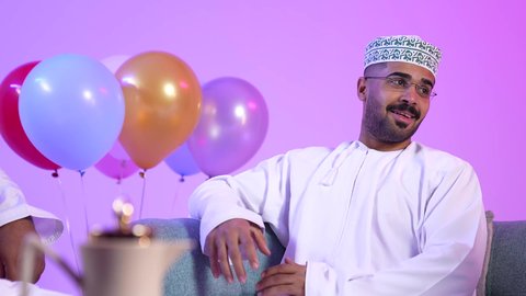Omani family gathering to welcome Eid, the concept of tenderness, love and affection, showing feelings of joy and happiness with the arrival of Eid, offering Saudi dates, offering Arab hospitality and traditional sweets, exchanging greetings, a picture of an Omani Gulf Arab family sitting in the living room with gestures of happiness