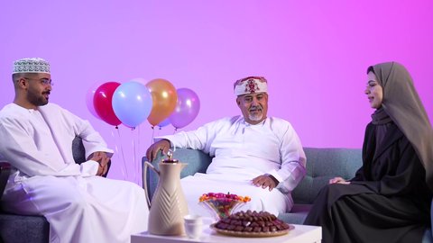 إظهار مشاعر الفرح والسعادة بقدوم العيد، تقديم التمر السعودي ، تجمع العائلة العمانية لاستقبال العيد المبارك, تقديم الضيافة العربية والحلويات الشعبية، تبادل المعايدات, مفهوم الحنان والمحبة والمودة، تصوير لعائلة عربية خليجية عمانية تجلس في غرفة المعيشة بايماءات السعادة