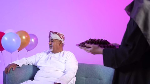 تقديم التمر السعودي ، تجمع العائلة العمانية لاستقبال العيد المبارك, تقديم الضيافة العربية والحلويات الشعبية، تبادل المعايدات, مفهوم الحنان والمحبة والمودة، إظهار مشاعر الفرح والسعادة بقدوم العيد، تصوير لعائلة عربية خليجية عمانية تجلس في غرفة المعيشة بايماءات السعادة