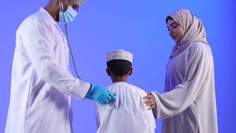 تصوير لأم عربية خليجية عمانيه مع طفلها  في زيارة الى دكتور الأطفال ، موعد مع الطبيب لتلقي العلاج ، مستشفى خاص بالأطفال ، مفهوم الطب والرعاية الصحية ، الفحص الطبي للأطفال ، الرعاية الطبية للأطفال ، يستمع الطبيب لقلب الطفل عبر سماعة الأذن