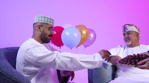 تجمع العائلة العمانية لاستقبال العيد المبارك, تقديم الضيافة العربية والحلويات الشعبية، تبادل المعايدات, مفهوم الحنان والمحبة والمودة، إظهار مشاعر الفرح والسعادة بقدوم العيد، تصوير لعائلة عربية خليجية عمانية تجلس في غرفة المعيشة بايماءات السعادة