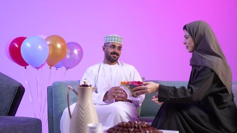تقديم الضيافة العربية والحلويات الشعبية، تجمع العائلة العمانية لاستقبال العيد المبارك, الزينة والبلالين والاحتفالات، تبادل المعايدات, مفهوم الحنان والمحبة والمودة، إظهار مشاعر الفرح والسعادة بقدوم العيد، تصوير لعائلة عربية خليجية عمانية تجلس في غرفة المعيشة بايماءات السعادة