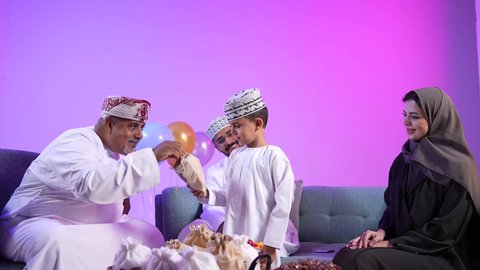 إظهار مشاعر الفرح والسعادة بقدوم العيد، تقديم الضيافة العربية والحلويات الشعبية، تجمع العائلة العمانية لاستقبال العيد المبارك, الزينة والبلالين والاحتفالات، تصوير لعائلة عربية خليجية عمانية تجلس في غرفة المعيشة بايماءات السعادة ، تبادل المعايدات, مفهوم الحنان والمحبة والمودة