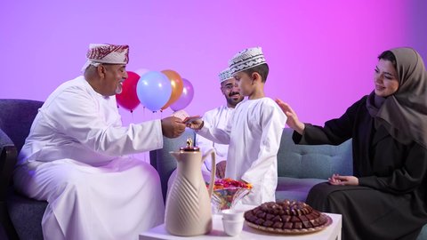 الزينة والبلالين والاحتفالات، تجمع العائلة العمانية لاستقبال العيد المبارك, إظهار مشاعر الفرح والسعادة بقدوم العيد، تصوير لعائلة عربية خليجية عمانية تجلس في غرفة المعيشة بايماءات السعادة ، تبادل المعايدات, مفهوم الحنان والمحبة والمودة، تقديم الضيافة العربية والحلويات الشعبية
