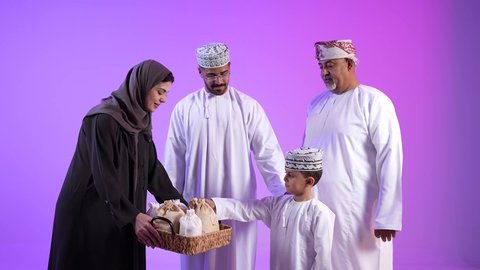 تجمع العائلة العمانية لاستقبال العيد المبارك, إظهار مشاعر الفرح والسعادة بقدوم العيد، الزينة والبلالين والاحتفالات، تصوير لعائلة عربية خليجية عمانية تجلس في غرفة المعيشة بايماءات السعادة ، تبادل المعايدات, مفهوم الحنان والمحبة والمودة، تقديم الضيافة العربية والحلويات الشعبية