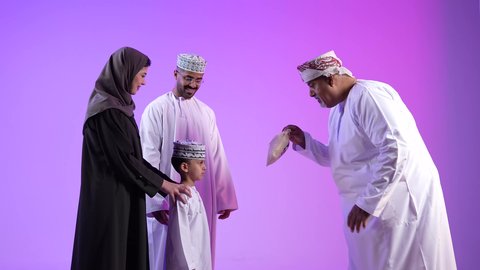 طقوس الاحتفالات والمناسبات السعيدة في سلطنة عمان، تبادل المعايدات في الأعياد، عائلة عربية خليجية عمانية تحتفل بالعيد المبارك، إظهار مشاعر الفرح والسعادة، خلفية ملونة