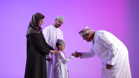 تبادل المعايدات في الأعياد، طقوس الاحتفالات والمناسبات السعيدة في سلطنة عمان، عائلة عربية خليجية عمانية تحتفل بالعيد المبارك، إظهار مشاعر الفرح والسعادة، خلفية ملونة