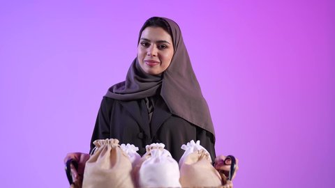 ارتداء الثياب الجديدة وأجواء البهجة في العيد, تصوير لامراه عربية خليجية عمانية تحتفل بالأعياد الاسلامية, الوقوف والنظر للكاميرا بإيماءات السعادة والفرح، تقديم الحلويات التقليدية والمأكولات الشهية, إظهار مشاعر المودة والمحبة العائلية, خلفية ملونة