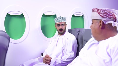 الحوار والنقاش مع الاصدقاء، قضاء الاوقات الممتعه ، تصوير مقرب من الجانب لرجلان عربييان عمانييان يرتديان الزى العمانى يجلسان على كراسي الطائره في رحله جويه يتبادلان الحديث