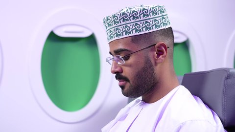 الاستمتاع باجازه الصيف ، قضاء الاوقات الممتعه ، تصوير مقرب من الجانب لرجلان عربييان عمانييان يرتديان الزى العمانى يجلسان على كراسي الطائره في رحله جويه