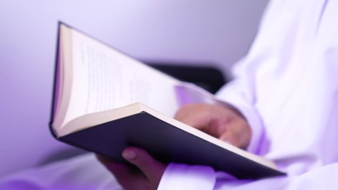 ممارسه الانشطه الترفيهيه وهوايه المطالعه, تصوير مقرب من الجانب لرجل عربي خليجي عماني يرتدي الدشداشه والكمه يجلس على كرسيه داخل الطائره يقرأ كتابا بيده, الطيران العماني الخليجي