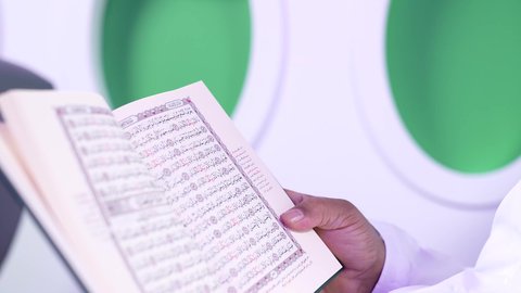 الترفيه والتسليه وقضاء الاوقات داخل الطائره, الاستمتاع بقرائه القصص والروايات, ممارسه الهوايات المفضله ، تصوير مقرب من الجانب لرجل عربي خليجي عماني بدين يرتدي الزي العماني يجلس على كراسي الطائره في رحله جويه يقرأ الرجل كتابا