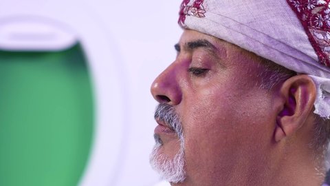 الاستمتاع بقرائه القصص والروايات, ممارسه الهوايات المفضله ، الترفيه والتسليه وقضاء الاوقات داخل الطائره, تصوير مقرب من الجانب لرجل عربي خليجي عماني بدين يرتدي الزي العماني يجلس على كراسي الطائره في رحله جويه يقرأ الرجل كتابا