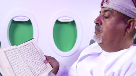 ممارسه الهوايات و الاستمتاع بقرائه القصص والروايات, الترفيه والتسليه وقضاء الاوقات داخل الطائره, جو، تصوير مقرب من الجانب لرجل عربي خليجي عماني بدين يرتدي الزي العماني يجلس على كراسي الطائره في رحله جويه يقرأ الرجل كتابا