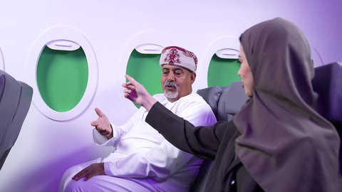 Discussion and dialogue between the family, entertainment and fun and spending time inside the plane, a close-up of an obese man and an Arab woman from the Gulf of Oman sitting on the plane seats on a flight
