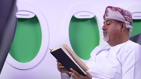 الاستمتاع بالقراءه والثقافه ، ممارسه الهوايات المفضله, الترفيه والتسليه وقضاء الاوقات داخل الطائره ، تصوير مقرب من الجانب لرجل بدين وامرأه عربيان خليجيان عمانيين يرتديان الزي العماني يجلسان على كراسي الطائره في رحله جويه