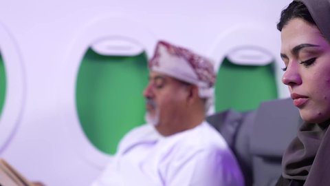 ممارسه الهوايات المفضله, الترفيه والتسليه وقضاء الاوقات داخل الطائره ، تصوير مقرب من الجانب لرجل بدين وامرأه عربيان خليجيان عمانيين يرتديان الزي العماني يجلسان على كراسي الطائره في رحله جويه