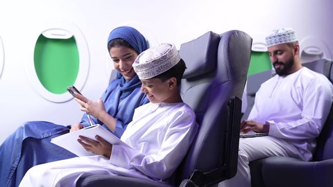 التنزه وقضاء الاوقات السعيده ، طفل يقضي وقت الرحلة في مشاهده الرسومات،تصوير لامرأة عربية عمانية خليجية برفقة ولدها في الطائرة، قضاء العطلة الصيفية برفقة العائلة، خطوط الطيران العماني