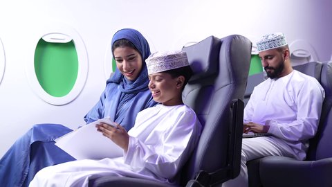 مفهوم السياحة و السفر، طفل يقضي وقت الرحلة في مشاهده الرسومات،تصوير لامرأة عربية عمانية خليجية برفقة ولدها في الطائرة، قضاء العطلة الصيفية برفقة العائلة، خطوط الطيران العماني