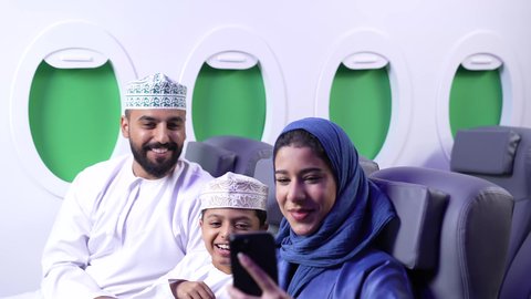 توثيق اللحظات المميزة باستخدام الأجهزة التقنية الحديثة, فعاليات و نشاطات مع الأسرة, قضاء الأوقات الممتعة مع الأبناء، الاستمتاع بالاجازة الصيفية ، تصوير مقرب لعائله عربيه خليجيه عمانية يرتدون الزي التقليدي يجلسون في الطائرة و يقومون بالتقاط صورة سيلفي