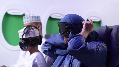 الحاجه الى الراحه و النوم ، قضاء اجازه صيفية ممتعه ، تصوير لعائله عربيه خليجيه عمانية يرتدون الزي التقليدي يجلسون في الطائرة ، امراة خليجيه ترتدي العباءة الزرقاء تقوم بارتداء قناع النوم