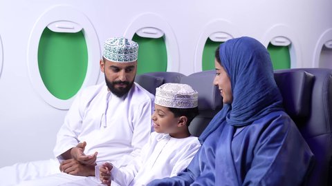 النقاش والحوار بين العائله ، الترفيه والتسليه وقضاء الاوقات داخل الطائره ، تصوير لعائله عربيه خليجيه عمانية يرتدون الزي التقليدي  يجلسون على كراسي الطائره في رحله جويه، قضاء الاجازه الصيفية