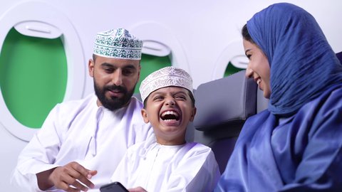 Gestures of happiness and pleasure, close-up of an Omani Gulf Arab family wearing traditional dress inside the plane with their son, family trips, hospitality, airlines, tourism and travel, tourist trip, traveling with family