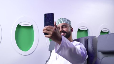 التقاط صورة شخصية تذكارية, استخدام التقنيات التكنولوجية الحديثة والمتطورة, إيماءات السعادة و السرور، تصوير مقرب لرجل عربي خليجي عماني يرتدي الدشداشه و الكمه يقوم بأخذ لقطة سيلفي عبر الهاتف المحمول داخل الدائرة ، رحلة سياحية من خلال خطوط الطيران العماني
