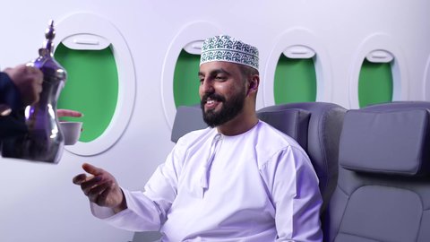 حسن الضيافة والاستقبال، قضاء العطلة الصيفية، تصوير مقرب ليد مضيفة الطيران تقوم بتقديم المشروبات الساخنة لركاب الطائرة،رجل عربي خليجي عماني يرتدي الدشداشة و الكمه يجلس على كرسيه داخل الطائره يقوم بتناول المشروب، خطوط الطيران العماني